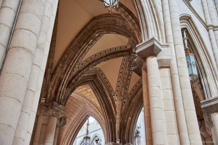 Almudena Cathedral, Madrid A close-up view of the interior arches and columns of a Gothic-style cathedral, featuring pointed vaults with colourful decorative patterns and stone detailing.