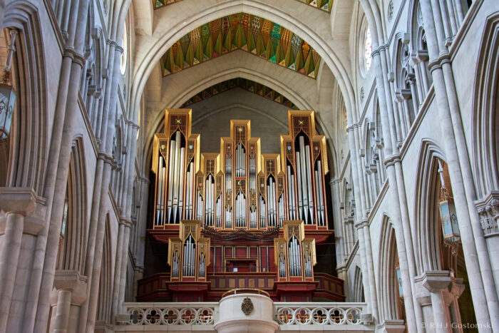 Almudena Cathedral, Madrid A grand pipe organ with gold and red accents is set against the stone interior of a cathedral, featuring high vaulted ceilings and intricate architectural details.