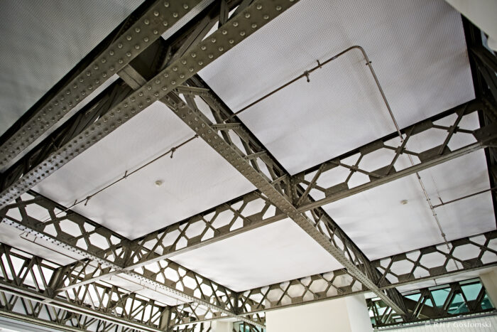 Palacio de Cibeles, Madrid Exposed industrial ceiling with metal beams and trusses, featuring white panels and visible wiring, in a modern interior space with natural light.