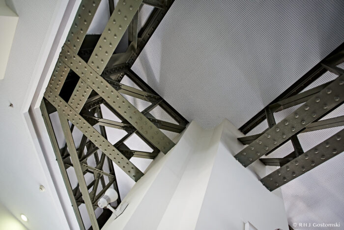 Palacio de Cibeles, Madrid A view looking up at the metal framework and beams supporting a ceiling, intersecting above a white structural pillar in a modern building.