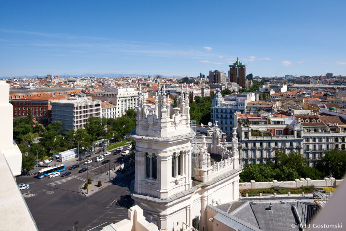 Palacio de Cibeles, Madrid Aerial view of Plaza de Cibeles in Madrid, featuring ornate white buildings, a busy junction, and cityscape with distant mountains under a clear blue sky.