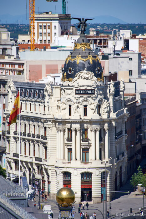 Palacio de Cibeles, Madrid The ornate Metropolis Building in Madrid, Spain, featuring a black dome topped with a winged statue, stands prominently among surrounding city buildings under a clear blue sky.