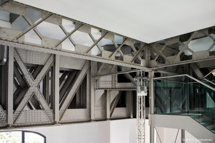 Palacio de Cibeles, Madrid Metal beams and riveted iron framework of the Eiffel Tower are visible inside a modern interior, with glass and metal stairs and railings at the lower right. Bright natural light fills the space.