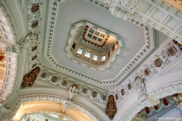 Palacio de Cibeles, Madrid Ornate ceiling with intricate white mouldings, decorative shields, and a central octagonal skylight with windows, viewed from below. The architecture features classical and baroque elements.