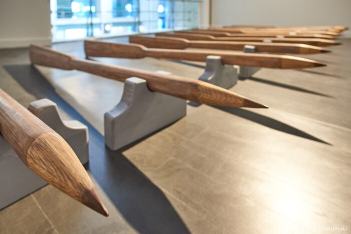 Palacio de Cibeles, Madrid Several large, pointed wooden stakes are arranged in rows on grey supports in a brightly lit indoor space with a window in the background.
