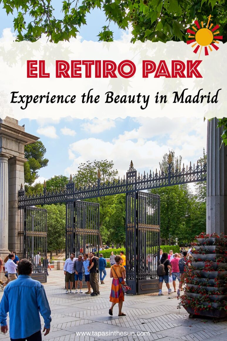 People gather near the large, ornate iron gates and stone pillars at the Entrance to Parque del Retiro in Madrid, surrounded by lush green trees on a sunny day. Some are walking, while others stand and talk in small groups.