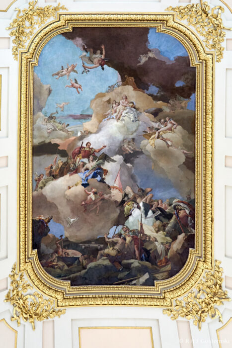 The Royal Palace, Madrid Ornate ceiling fresco with angels, cherubs, and classical figures among clouds, surrounded by an elaborate gold frame in a grand interior. The scene features dynamic poses and vibrant colours, evoking a mythological or celestial event.