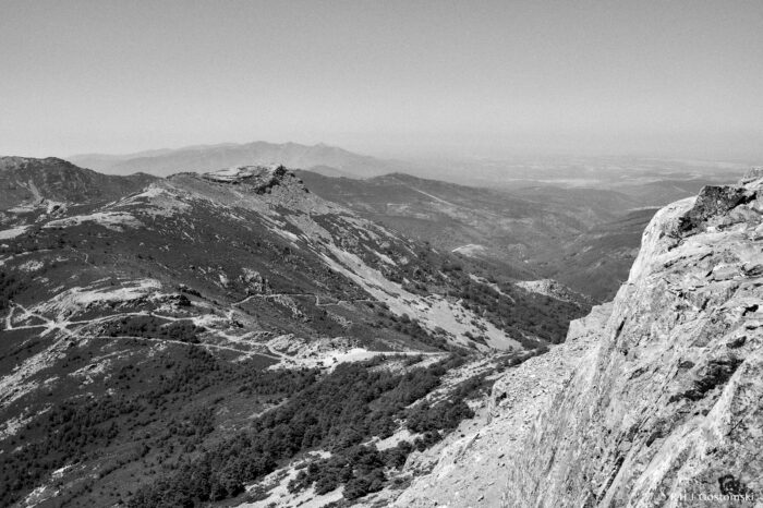 Views of the Sierra de Francia Black and white photo of the Sierra de Francia - a rugged mountain landscape with rocky peaks, tree-covered slopes, winding paths, and distant hills under a clear sky.
