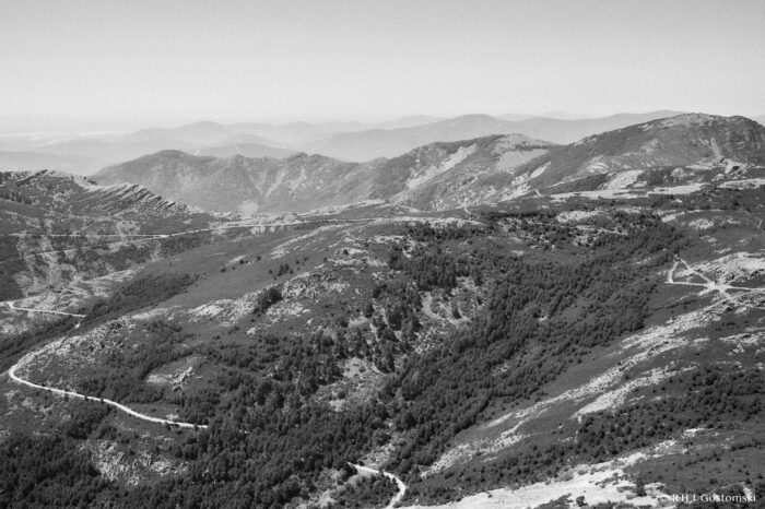 Views of the Sierra de Francia Black and white photo of the Sierra de Francia - a mountainous landscape with winding dirt roads, scattered trees, and distant mountain ranges fading into the horizon under a clear sky.