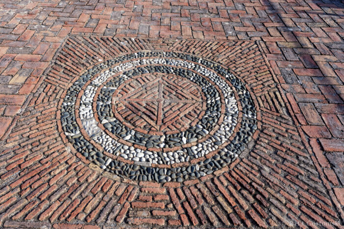 Ornate pebble setts at Castillo Gibralfaro A circular stone mosaic with a star pattern in the centre, made of white, black, and grey stones, set within a square section of red bricks, surrounded by a herringbone brick pattern.