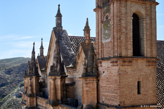Close-up view of the historic Royal Collegiate Church of Santa María la Mayor, showcasing its pointed Gothic arches and spires, set against a hillside under a clear blue sky.