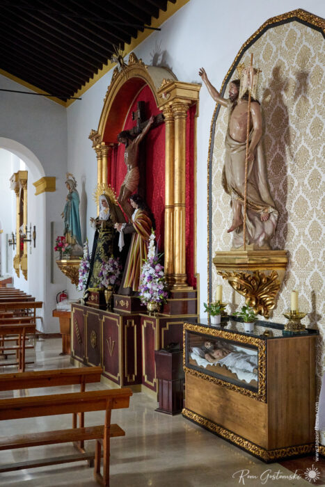 Inside Parroquia Nuestra Se&ntilde;ora de la Asunci&oacute;n, wooden pews, religious statues, and ornate gold-trimmed altars adorned with flowers create a serene atmosphere. Statues of Jesus on the cross, the Virgin Mary, and another saint stand prominently displayed.