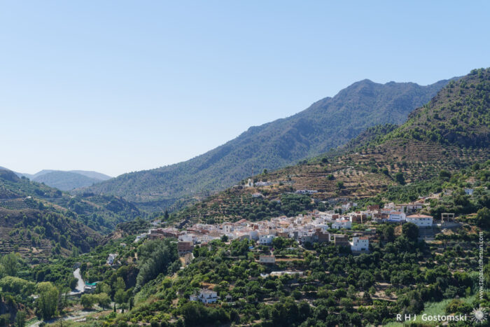 The neighbouring village, Guájar-Fondón The small whitewashed village of Guájar-Fondón nestles among green trees and terraced hillsides beneath clear blue skies, surrounded by mountains.