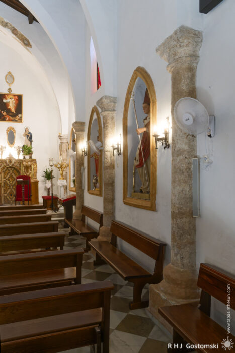 Inside Iglesia San Lorenzo Inside Iglesia San Lorenzo, a view reveals wooden pews, arched stone columns, religious statues in ornate frames along the wall, and soft wall lighting. An altar decorated with gold accents is visible in the background.