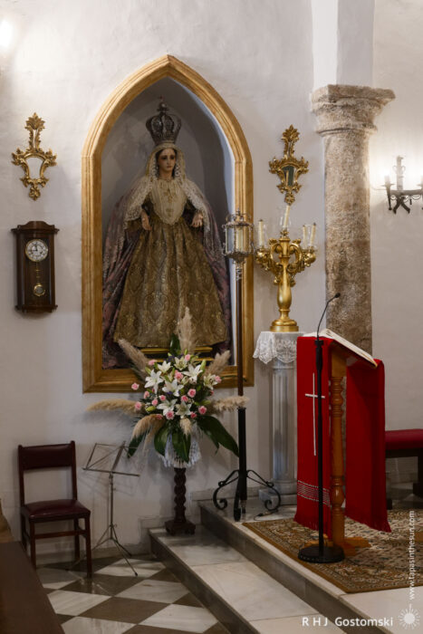 Inside Iglesia San Lorenzo Inside Iglesia San Lorenzo, a statue of the Virgin Mary dressed in ornate robes stands in a niche, surrounded by flowers and lit candles. Nearby are a pulpit with a red cloth, a gold lectern, a clock, and a column.