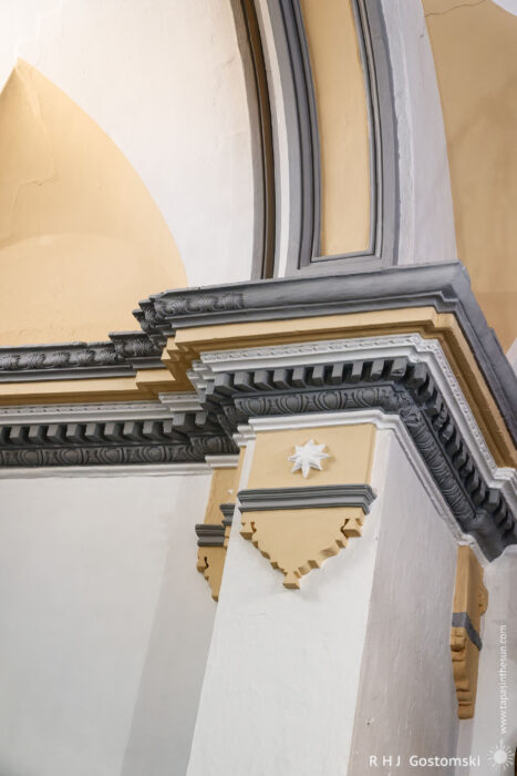Elegant Architectural Detail of a Column in Santo Domingo de Guzmán Church An architectural detail featuring a gray and yellow column with intricate molding and a star decoration, set against a softly illuminated wall. The design highlights the craftsmanship in the building's interior.
