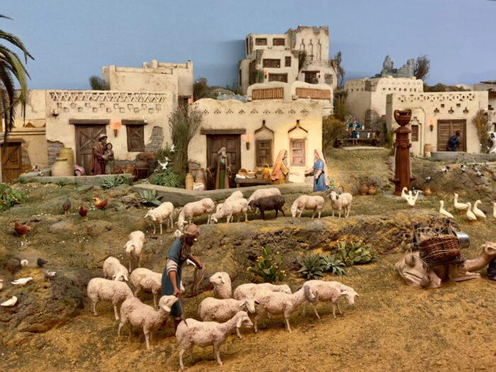 Part of the Bel&eacute;n -  A detailed nativity scene featuring figures of a marketplace with livestock. People are engaged in various activities, surrounded by palm trees and traditional buildings, capturing a historical or biblical setting.
