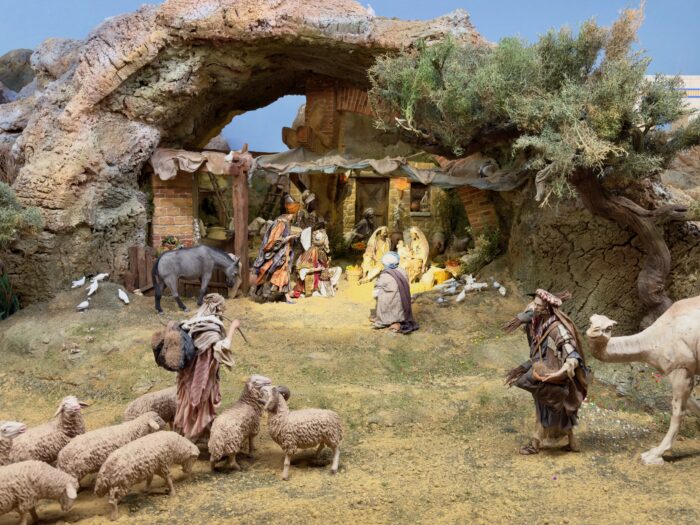 Part of the Bel&eacute;n -  A detailed nativity scene featuring the Holy Family inside a cave, surrounded by shepherds, sheep, and various animals, set in a pastoral landscape with greenery, highlighting the birth of Jesus.